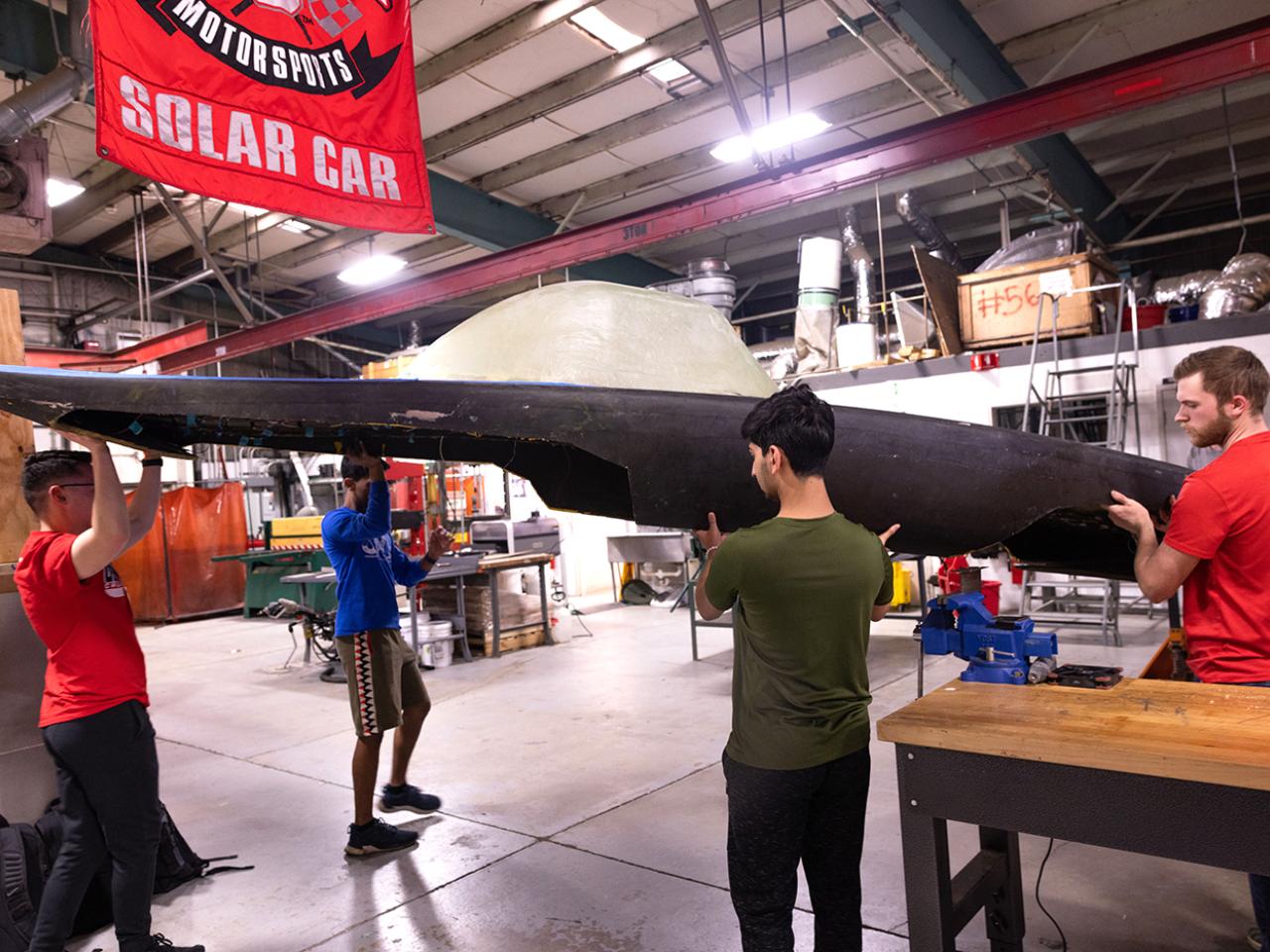 Jasper Hu, Atish Anantharan, Ritvik Rao and Sean Pitzer carry the Buckeye Solar Car outside at the Center for Automotive Research