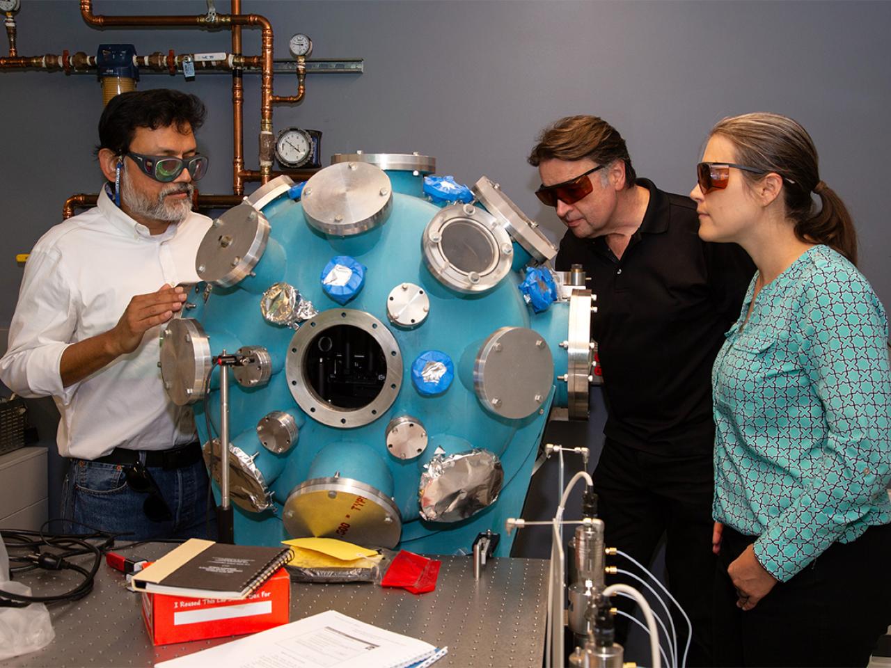 Three people studying a structure for performance and critical evaluation of materials in Low Earth Orbit (SPACE-MAT) Center of Excellence