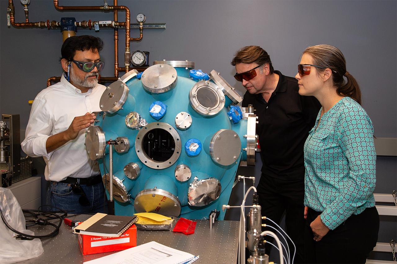 Three people studying a structure for performance and critical evaluation of materials in Low Earth Orbit (SPACE-MAT) Center of Excellence