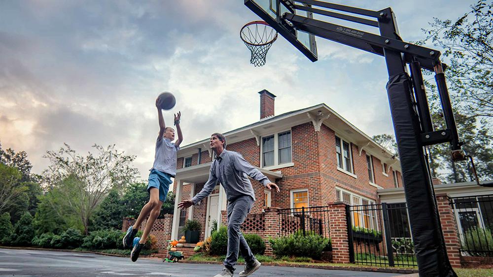 Byron shooting a ball into a basketball net while playing with his dad.